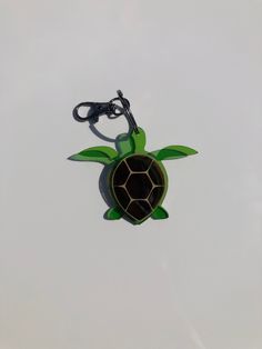 a green turtle shaped keychain hanging from a black hook on a white background