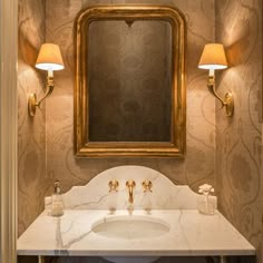 a bathroom with a marble counter top and gold framed mirror above the sink, along with two lamps on either side