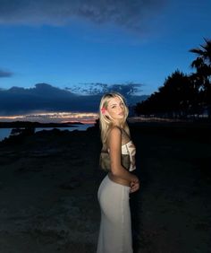 a woman standing on top of a sandy beach next to the ocean at night time