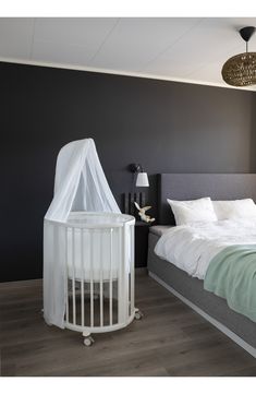 a white crib next to a bed in a room with dark walls and wooden floors