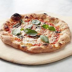 a pizza sitting on top of a wooden plate covered in cheese and basil leaf toppings