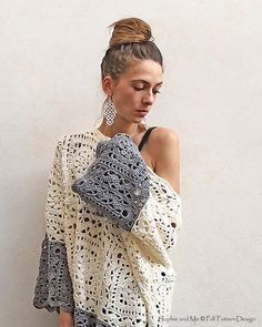 a woman standing in front of a white wall with her hand on her shoulder and wearing a crocheted sweater