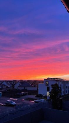 the sun is setting over a parking lot with cars parked in front of it and buildings on either side