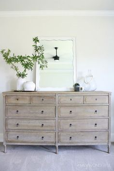 a dresser with two plants on top and a mirror above it