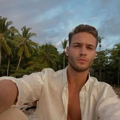 a man in white shirt sitting on beach next to palm trees