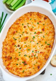 a casserole dish with cheese and green onions next to bread, celery and tomatoes