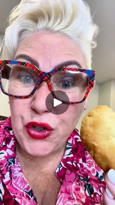 an older woman holding a doughnut in her hand and looking at the camera while wearing glasses