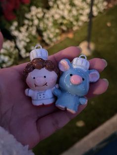 a person is holding two small figurines in their hand with flowers behind them