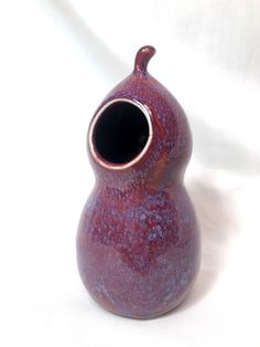 a red vase sitting on top of a white table next to a black object with a hole in it