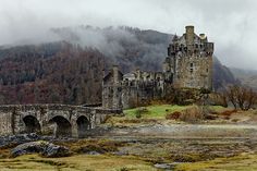 an old castle sits in the middle of a field with trees and mountains behind it