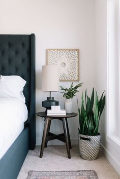 a bed room with a neatly made bed next to a night stand and potted plants