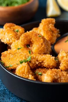 a black bowl filled with fried vegetables and dipping sauce