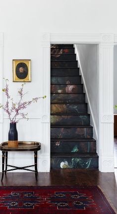 a vase with flowers on top of a table next to a stair case and rug