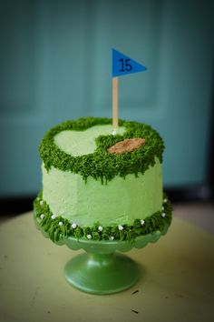 a green cake decorated with grass and a blue flag