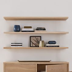 two wooden shelves with books and vases on them in front of a white wall