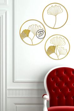 three decorative wall art pieces in gold and silver on a white wall next to a red chair