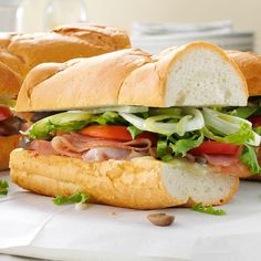 two sub sandwiches with meat, lettuce and tomato on them sitting next to each other