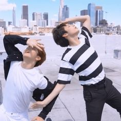 two young men standing next to each other in front of a cityscape with skyscrapers