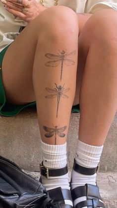 a woman sitting on the ground with her legs crossed and dragonfly tattoo on her leg