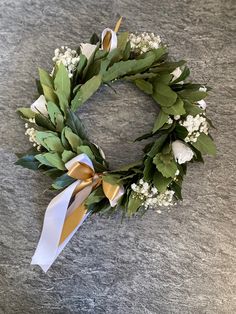 a wreath with white flowers and green leaves on a gray table top, ready to be used as an ornament