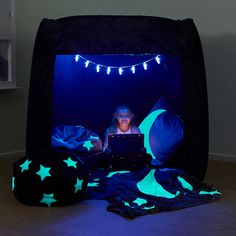 a child is sitting in a tent with stars and moon lights on it while using a laptop