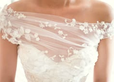 a woman wearing a white wedding dress with flowers on the bottom and veil over her shoulder