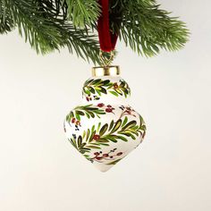 a white ornament hanging from a christmas tree with green leaves and red berries