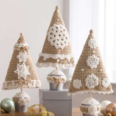 three crocheted christmas trees sitting on top of a wooden table next to ornaments