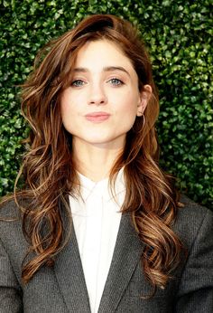 a woman with long brown hair wearing a suit and white shirt in front of a green wall