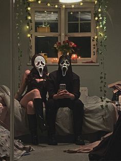 two people in masks sitting on a bed looking at their cell phones