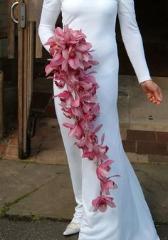 a woman wearing a white dress with pink flowers on the side and long sleeves, standing in front of a door