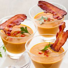 three glasses filled with soup and bacon on top of each other, sitting on a table