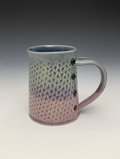 a blue and purple coffee mug sitting on top of a white table next to a gray wall