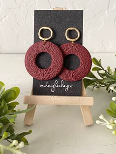 two pairs of red and black leather earrings with gold hoop closures on a wooden stand