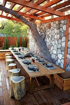 a wooden table with plates and bowls on it in front of a stone wall under a tree