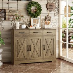 a wooden cabinet sitting in front of a window next to a potted plant and pictures on the wall