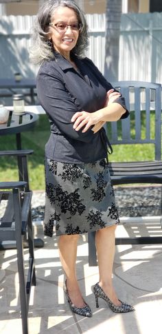 an older woman standing with her arms crossed in front of a table and bench outside