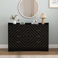 a black and gold dresser with a round mirror on the wall above it, next to a lamp