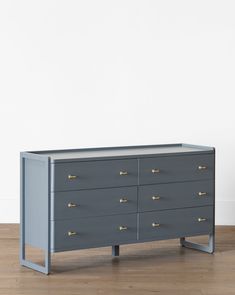 a grey dresser with gold handles and drawers on the bottom, in front of a white wall