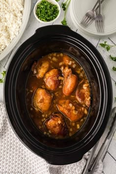 a crock pot filled with chicken and beans on top of a table next to rice