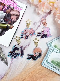 some anime key chains are laying on top of a table next to money and flowers