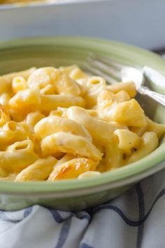 a green bowl filled with macaroni and cheese on top of a blue towel