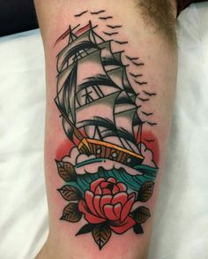 a tattoo on the leg of a man with a ship and rose in it's center