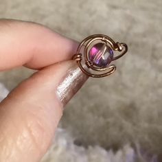 a woman's hand holding a ring with a pink stone in the middle and a wire wrapped around it