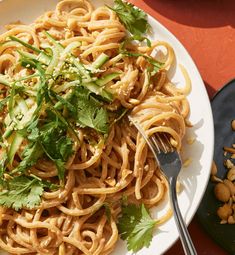 a white plate topped with noodles and veggies next to a bowl of peanuts