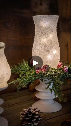 three white vases with pine cones and greenery in them on a wooden table