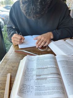 a man sitting at a table with an open book and pen in his hand while writing on paper