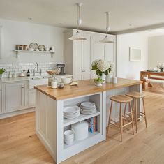 an open kitchen with white cabinets and wooden counter tops, along with two stools in front of the island