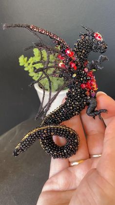 a hand is holding a tiny lizard made out of beads and other things in it