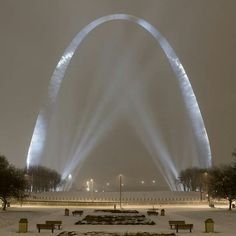 an arch lit up in the night with snow on the ground and benches around it